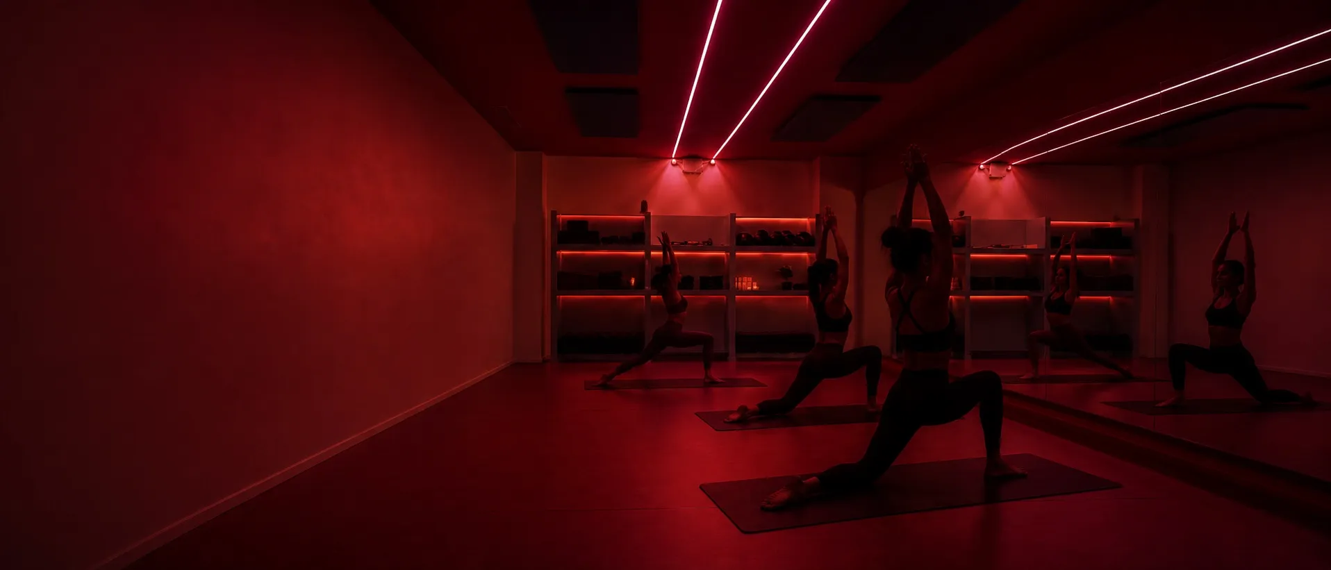 La salle du studio en lumière rouge : trois élèves en fente haute sur leur tapis, face au miroir.